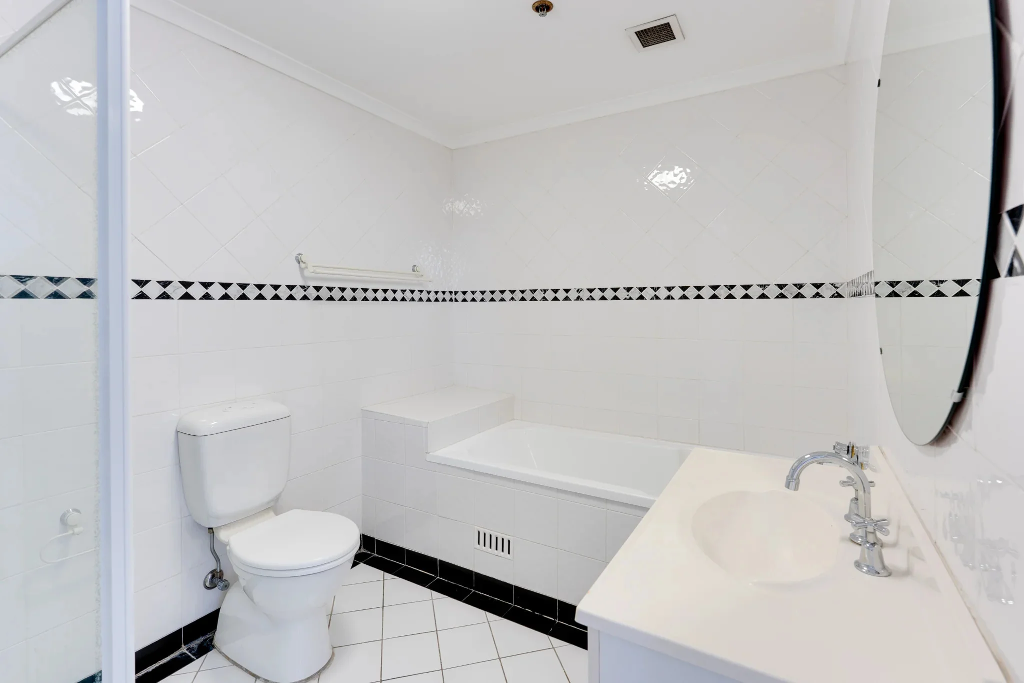 An empty bathroom before staging: bare vanity, an unadorned tub ledge, and an empty towel rail.