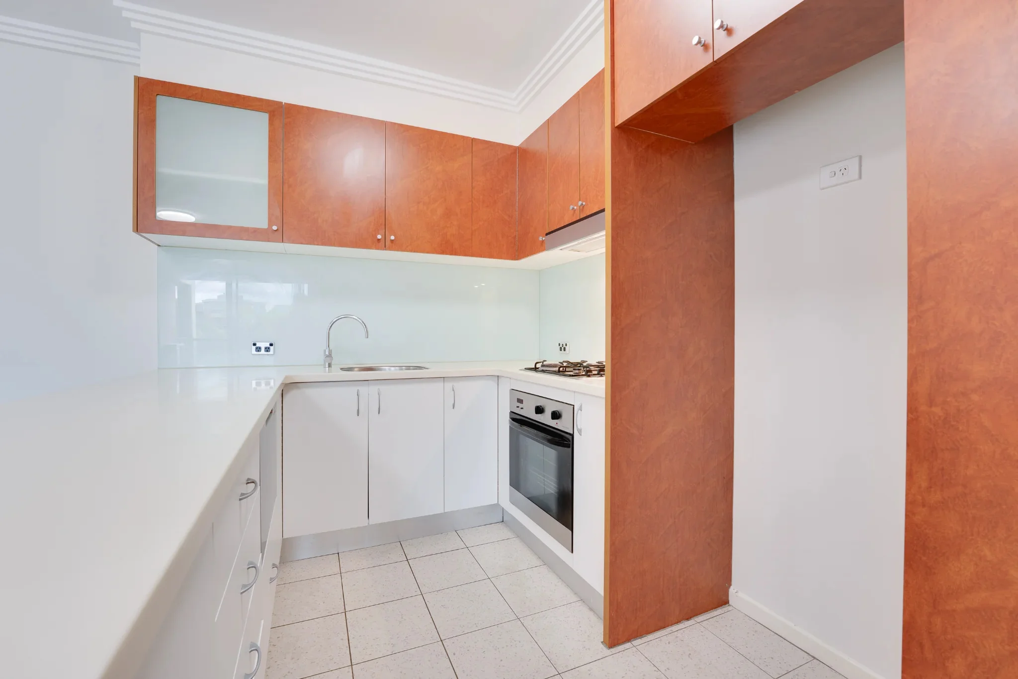 An empty kitchen before staging: bare countertops, glass splashback, and existing cabinetry.