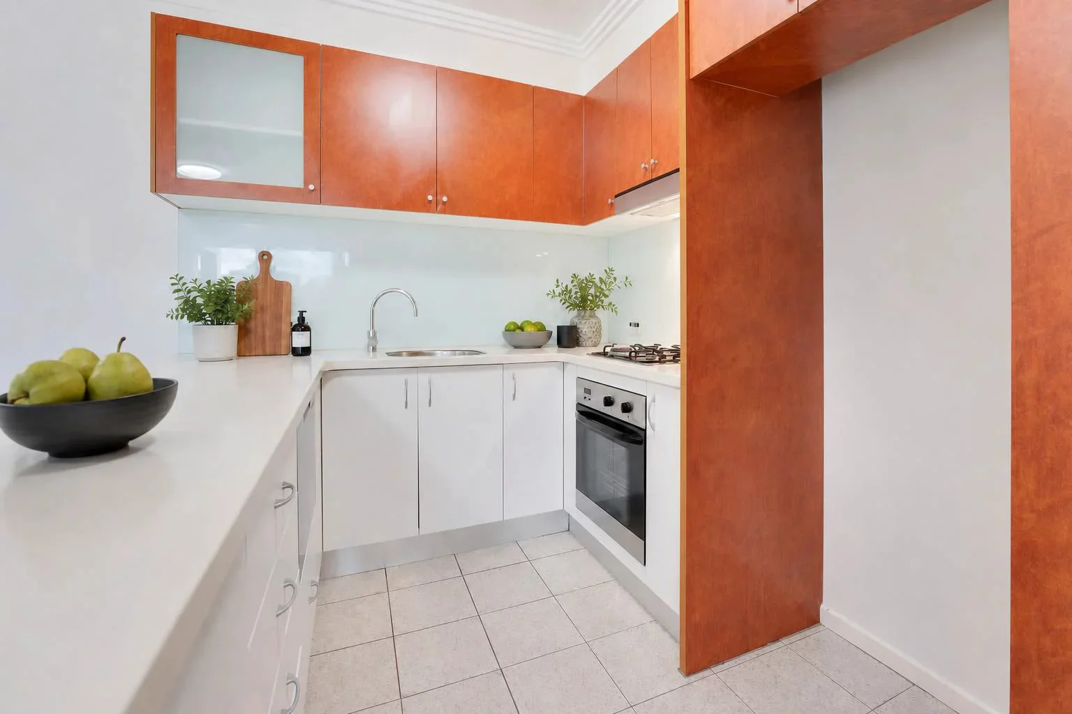 The same kitchen styled with SecondLight: greenery, a board, and fruit bowls added to the counters while the cabinetry, appliances, and splashback stay exactly as they were.